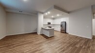 This two-story space is designed with a clean, contemporary aesthetic throughout, combining functionality with modern finishes. The main level features an open-concept layout where the living area flows seamlessly into the kitchen. Wide-plank hardwood-style flooring runs throughout this level, complementing the neutral gray walls and recessed lighting overhead. Natural light enters through multiple windows fitted with horizontal blinds.

The kitchen is well-appointed with white shaker-style cabinetry, light quartz countertops, and a geometric tile backsplash. Stainless steel appliances include a slide-in range, over-the-range microwave, and dishwasher. A peninsula with an undermount sink adds prep space and casual seating potential. A compact half bath on the main level features a pedestal sink and tile flooring, offering a clean, minimalist design.

The upper level houses the bedrooms, each finished with plush neutral carpet and neutral-toned walls. A full bathroom serves the upper level, featuring a white vanity with quartz countertop, a large mirror, and a walk-in glass-enclosed shower with tile surround. A dedicated laundry room on the upper level includes a full-size washer and dryer. The overall ambiance is fresh, move-in ready, and cohesively modern.