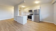 This well-appointed one-bedroom, one-bathroom unit is located in Toronto's M6L neighbourhood and offers a thoughtfully designed single-floor layout. Light wood laminate flooring runs throughout the space, complementing the clean, neutral colour palette found in every room. The open-concept living area is generously sized, bathed in natural light through a wide bank of windows that run along the exterior wall, with baseboard heating positioned beneath. The space connects seamlessly to a modern kitchen featuring white shaker-style cabinetry, a central island with a white quartz countertop, stainless steel appliances including a fridge, range, and over-the-range microwave, and a sink with a tiled backsplash. The bedroom offers a comfortable footprint, natural light from a dedicated window, and a built-in sliding-door closet. The bathroom is finished with white subway tile surrounding the soaker tub and shower, a white undermount vanity sink, and chrome fixtures. Additional features include an entrance foyer, an in-unit laundry area, and a private balcony. The overall ambiance is clean, bright, and move-in ready.