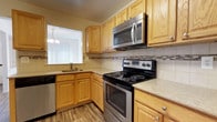 Located at 1200 Charleston Greene in Malvern, Pennsylvania, this two-story residence offers a thoughtfully designed layout across two levels. The kitchen is a standout feature, showcasing warm honey-toned wood cabinetry that extends to the ceiling, providing generous storage throughout. A decorative tile backsplash with a mosaic accent border adds a refined touch to the space. Stainless steel appliances — including an electric range, over-the-range microwave, and dishwasher — complement the light-toned countertops. A sink positioned beneath a window allows for natural light to fill the workspace, and a pendant light fixture overhead adds a decorative element to the area. The kitchen's wood-look flooring ties the warm tones of the cabinetry together cohesively. The two-floor layout of the home offers separation between living and private spaces, contributing to a functional and comfortable flow throughout. The overall design aesthetic is classic and inviting, with practical finishes that balance everyday utility with an approachable warmth suited to the Malvern community setting.