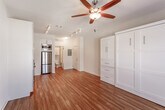 This single-floor studio unit at 7979 Metcalf Ave in Overland Park, Kansas offers a smart, open layout enhanced by warm hardwood flooring throughout. The main living area is anchored by a built-in Murphy bed system with crisp white cabinetry, integrated shelving, and drawer storage — maximizing functionality without sacrificing floor space. A ceiling fan with light fixture keeps the area comfortable, while French doors on one end of the room invite natural light and provide access to a private balcony.

The kitchen is efficiently designed with white cabinetry, open floating shelves, grey countertops, and a full suite of stainless steel appliances, including a range, dishwasher, built-in microwave, and a full-size refrigerator. Track lighting overhead illuminates the workspace effectively.

The bathroom area extends into a hallway that connects to an in-unit laundry closet with a stacked washer and dryer, offering added convenience. The vanity features grey countertops and modern hardware consistent with the unit's clean, contemporary aesthetic. The overall design balances practicality with a bright, neutral palette.