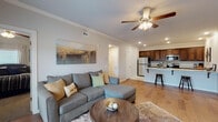 Located at 259 S Maestri Rd in Tontitown, Arkansas, this single-floor residence offers a thoughtfully designed open-concept layout that seamlessly connects the living, dining, and kitchen areas. The living room features warm hardwood-style flooring, crown molding, a ceiling fan with light fixture, and French doors that invite natural light and provide access to an outdoor balcony. The kitchen is a standout, equipped with rich dark wood cabinetry, granite countertops, stainless steel appliances including a refrigerator, range, and microwave, and a peninsula island with an undermount sink and bar seating for two — ideal for casual dining or entertaining. The bedrooms are carpeted for comfort, each featuring ceiling fans, ample natural light from plantation-shuttered windows, and neutral tones that create a calm, restful atmosphere. One bedroom includes a tufted upholstered headboard wall and space for a desk, offering versatility. The bathroom presents granite-topped dark wood vanity cabinetry, tile flooring, and a full tub-shower combination. Throughout the unit, crown molding, recessed lighting, and a cohesive neutral color palette lend a polished, modern feel to the overall space.