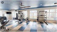 Located at 3830 NC-55 E in Durham, NC, this fitness center offers a spacious, single-floor layout designed to support a comprehensive workout experience. The room's most striking design element is the bold navy blue ceiling, which contrasts sharply with the crisp white walls and creates a dynamic, energizing atmosphere. Underfoot, a large-scale blue and tan checkered resilient tile floor adds a distinctive visual character while providing durability and easy maintenance.

Natural light pours in through multiple large windows along the walls, offering views of the surrounding community and keeping the space feeling open and inviting. Overhead, ceiling fans paired with sleek linear LED lighting fixtures ensure the room remains comfortable and well-illuminated throughout the day.

The fitness center is comprehensively equipped for a full range of workouts. A row of cardio machines — including treadmills, ellipticals, a stair climber, and a rowing machine — lines one side of the floor. On the strength training side, a multi-station cable machine, a Smith machine, a dumbbell rack with adjustable bench, medicine balls, kettlebells, and a punching bag provide extensive options for resistance training. A wall-mounted mirror near the free weights area enhances the sense of space, while a water fountain station near the entrance ensures convenient hydration. Wall-mounted TVs are positioned throughout for entertainment during workouts.