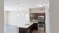 This 2-bedroom, 2-bathroom unit in Leander, Texas offers a thoughtfully designed single-story layout that balances functionality with modern style. The open-concept kitchen and living area forms the heart of the unit, anchored by a central island with granite countertops, a double undermount sink, and pendant lighting overhead. The kitchen is outfitted with rich dark-espresso cabinetry, stainless steel appliances including an electric range and microwave, and a geometric mosaic tile backsplash that adds a contemporary touch. Wood-style flooring runs through the main living areas, contributing to a cohesive, clean aesthetic.

Both bedrooms are carpeted and feature ceiling fans and natural light from well-placed windows. The primary bedroom is generously sized and includes a walk-in closet with built-in shelving. A sliding glass door in one room opens to an outdoor view, while neutral wall tones throughout create a calm, versatile atmosphere. The bathrooms are finished with white tile tub-shower surrounds and clean, simple fixtures. A built-in closet with multi-tier shelving provides practical storage solutions. Overall, the unit presents a comfortable and modern living environment.