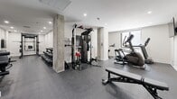 Located at 742 Rue William in Montréal's Saint-Henri district, this fitness facility offers a thoughtfully organized exercise space across a single floor. The gym features a contemporary design with crisp white walls, recessed lighting, and durable rubber-speckled flooring throughout, creating a clean and functional environment for training.

The space is divided into distinct workout zones. The strength training area is anchored by a power rack from Addict Fitness, accompanied by a multi-functional cable machine and a full rack of hex dumbbells spanning a wide range of weights, all neatly organized for easy access. Adjustable weight benches are positioned throughout to support a variety of exercises.

On the cardio side, the gym is equipped with treadmills, a stair climber, and a stationary bike, all positioned near a window that allows natural light to filter in. Exposed concrete structural columns add an industrial character to the space, complementing the otherwise modern aesthetic.

Large mirrors are strategically mounted along the walls, enhancing the sense of openness and allowing users to monitor their form during workouts. The layout is efficiently planned to maximize usability without overcrowding, making the most of the available floor area. Overall, this gym provides a well-rounded fitness environment suitable for both strength and cardiovascular training.