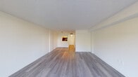 This single-floor residence offers a clean, functional layout designed for comfortable everyday living. The main living area is spacious and open, featuring light gray wood-style laminate flooring that runs throughout the space, crisp white walls, and a textured ceiling that adds subtle character. A large sliding glass door floods the living room with natural light and provides a pleasant outdoor view of surrounding greenery, creating a bright and airy atmosphere.

The kitchen is efficiently laid out and thoughtfully appointed, featuring white shaker-style cabinetry with modern hardware, light stone-look countertops, a stainless steel refrigerator, and a built-in dishwasher. A pass-through opening connects the kitchen to the living area, enhancing the sense of openness between the two spaces.

A hallway leads from the main living area to the rest of the unit, including the bathroom. The bathroom is clean and straightforward, equipped with a full-size soaking tub and shower combination, a toilet, and light-toned walls that maintain the consistent, neutral palette found throughout the home. The wood-style flooring continues into the bathroom, tying the interior together cohesively. Overall, the space presents a tidy, move-in-ready environment with a neutral design that offers a versatile backdrop for a variety of interior styles.