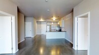 This single-floor space showcases a clean, modern aesthetic defined by its open-concept design and polished concrete flooring, which runs seamlessly throughout the main living area, reflecting light and adding an industrial-chic character to the interior. The layout connects the living area directly to the kitchen, creating a cohesive and functional flow.

The kitchen is a standout feature, equipped with stainless steel appliances, including a full-size refrigerator and built-in microwave. White cabinetry lines the upper and lower sections, complemented by dark countertops that provide a striking contrast. A peninsula with an integrated sink extends into the open space, offering both additional prep area and a casual seating opportunity. Above the peninsula, a series of pendant lights hang at varying heights, providing focused task lighting while enhancing the contemporary feel.

The neutral-toned walls throughout contribute to a bright, airy atmosphere, while recessed lighting supplements the pendant fixtures. Multiple doorways are visible, suggesting access to additional rooms or storage. The overall ambiance is minimalist and functional, with a modern industrial sensibility that gives the space a versatile, urban character.