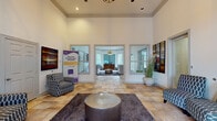 This leasing office in Memphis, Tennessee offers a polished and professional environment designed to make a strong first impression. The space is defined by its dramatic soaring ceilings adorned with crisp crown molding, creating an open and airy atmosphere that immediately conveys a sense of quality and scale.

The entry foyer greets visitors with warm-toned stone tile flooring that extends throughout the office, complemented by recessed lighting and a decorative pendant fixture overhead. Large double doors with an arched transom window flood the entrance with natural light, offering views of the surrounding greenery outside.

The main reception area is thoughtfully appointed with stylish accent chairs in geometric-patterned upholstery, a plush area rug anchoring a metallic drum coffee table, and curated abstract artwork displayed prominently on the walls. Tall decorative grasses in oversized white ceramic planters add organic texture to the refined interior.

French doors with glass panels open into a private interior office area, where a warm wood reception desk and additional seating create a comfortable consultation space. A cozy lounge alcove features a neutral-toned settee with nail-head trim detailing beneath a large-scale painting, adding an intimate touch to the space.

Throughout, the design strikes a balance between approachable warmth and sophisticated professionalism, making this leasing office an inviting destination for prospective residents.