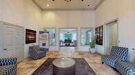 This leasing office in Memphis, Tennessee offers a polished and professional environment designed to make a strong first impression. The space is defined by its dramatic soaring ceilings adorned with crisp crown molding, creating an open and airy atmosphere that immediately conveys a sense of quality and scale.

The entry foyer greets visitors with warm-toned stone tile flooring that extends throughout the office, complemented by recessed lighting and a decorative pendant fixture overhead. Large double doors with an arched transom window flood the entrance with natural light, offering views of the surrounding greenery outside.

The main reception area is thoughtfully appointed with stylish accent chairs in geometric-patterned upholstery, a plush area rug anchoring a metallic drum coffee table, and curated abstract artwork displayed prominently on the walls. Tall decorative grasses in oversized white ceramic planters add organic texture to the refined interior.

French doors with glass panels open into a private interior office area, where a warm wood reception desk and additional seating create a comfortable consultation space. A cozy lounge alcove features a neutral-toned settee with nail-head trim detailing beneath a large-scale painting, adding an intimate touch to the space.

Throughout, the design strikes a balance between approachable warmth and sophisticated professionalism, making this leasing office an inviting destination for prospective residents.