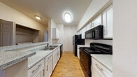 This single-floor residence offers a thoughtfully designed layout that balances functionality and comfort throughout its key living areas. The galley-style kitchen is a standout feature, showcasing crisp white cabinetry, speckled granite-look countertops, and a full suite of black appliances including a refrigerator, electric range, microwave, and dishwasher. Warm hardwood-style flooring runs underfoot, and a circular overhead light adds a distinctive touch to the space.

The open living and dining area is bright and welcoming, benefiting from natural light streaming through blinded windows and a glass-paneled door that leads to an outdoor space. The same warm hardwood-style flooring carries through these common areas, creating a cohesive and clean aesthetic.

The bedrooms offer a comfortable retreat, each featuring plush carpeting, ceiling fans with light fixtures, and windows dressed with blinds that allow for natural light control. Closet access is conveniently located within each room.

The bathroom is practical and well-appointed, featuring a wide vanity with speckled countertops, white cabinetry, a large mirror, and tiled walls. The overall ambiance of the residence is clean, neutral, and move-in ready, with a consistent design language throughout.