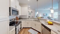 Located at 157 Hathaway Ln in Mooresville, NC, this well-appointed single-story home offers one bedroom, two full bathrooms, and a thoughtfully designed layout across a comfortable footprint. The open-concept kitchen is a standout feature, boasting granite countertops, a large island with pendant lighting, white shaker cabinetry, subway tile backsplash, and stainless steel appliances — ideal for both everyday cooking and entertaining. The kitchen flows into a dedicated dining area with warm hardwood-style flooring, and continues into a bright, welcoming living room. The living room is filled with natural light from large windows and a glass door that opens to the outdoors, creating an airy, inviting atmosphere. The spacious primary bedroom features plush carpeting, a ceiling fan, natural light from large windows, and direct access to a walk-in closet. Two full bathrooms serve the home: one features a subway tile tub/shower combination with brushed nickel fixtures, while the other includes a tiled walk-in shower, granite vanity, and white cabinetry. An in-unit laundry area with a full-size washer and dryer adds convenience. Throughout, neutral tones and clean finishes create a cohesive, move-in-ready aesthetic.