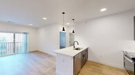 Located at 100 Mia Rose Way in Dardenne Prairie, MO, this thoughtfully designed one-bedroom, one-bathroom unit offers a clean, modern aesthetic throughout its efficiently utilized single floor. Light-toned hardwood flooring runs continuously through the space, complementing the crisp white walls and creating a bright, cohesive feel.

The open-concept kitchen and living area form the heart of the unit. The kitchen features a center island with a white quartz countertop, an undermount sink with a matte black faucet, and stylish dark pendant lighting overhead. Gray shaker-style cabinetry lines the walls, paired with stainless steel appliances including a refrigerator, range, and microwave, along with a classic tile backsplash.

The living area flows seamlessly from the kitchen and opens to a private balcony through a sliding glass door, offering outdoor views and additional natural light. The bedroom is a well-proportioned, serene retreat featuring multiple windows with blinds, a ceiling fan, and access to two closets. The bathroom is elegantly appointed with a marble-tiled walk-in shower, gray vanity cabinetry, a backlit mirror, and matching hardwood-style flooring. A utility room and hallway round out the practical layout of this well-appointed home.