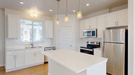 Located at 5959 Cougar Ln in Kearns, Utah, this contemporary three-story townhome offers a well-organized layout across three distinct levels. The ground floor provides a spacious attached garage with an automatic opener, offering secure parking and additional storage capacity.

The main living level serves as the heart of the home, featuring a bright, open-concept space that seamlessly integrates the living room, dining area, and kitchen. The kitchen is outfitted with white shaker-style cabinetry, a white quartz countertop island with pendant lighting, a full suite of stainless steel appliances, a subway tile backsplash, and a double-basin sink beneath a natural light-admitting window. Light hardwood-style flooring flows throughout this level, enhancing the clean, modern aesthetic. A pantry and convenient staircase access are also found on this floor.

The upper floor houses two bedrooms, including a well-proportioned primary bedroom, all featuring plush carpet flooring and ample closet space. Three full bathrooms are distributed across the home, each finished with white cabinetry, quartz countertops, and hardwood-style flooring. A private balcony on the top floor offers views of the surrounding community. Additional amenities include a dedicated laundry area and utility room, completing this functional and stylish multi-level home.