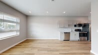 This thoughtfully designed single-floor unit offers a clean, contemporary aesthetic throughout, unified by light wood-style flooring and a soft neutral color palette. The open-concept living and kitchen area provides a generous, airy feel, with recessed lighting illuminating the space from above. The kitchen is well-appointed with white shaker-style cabinetry, stone-look countertops, a single-basin sink, and a full suite of stainless steel appliances including a refrigerator, electric range, over-the-range microwave, and dishwasher. A hallway connects the main living area to the private rooms, featuring a standout sliding barn door that adds a modern design touch alongside recessed lighting and a smart thermostat. The bedroom is generously sized, filled with natural light from a large multi-pane window with blinds, and includes two side-by-side closets with built-in rod shelving — offering excellent storage. An additional room provides flexible space with recessed lighting. The bathroom includes a full tub-shower combination with clean white surround finishes. Throughout the unit, crisp white trim, smooth walls, and consistent flooring create a cohesive, move-in-ready environment with a bright and welcoming ambiance.