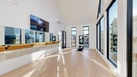 Located in Heber City, Utah, this contemporary fitness studio is a thoughtfully designed single-room space that balances functionality with striking architectural appeal. The studio's most commanding feature is its dramatic vaulted ceiling, which rises to impressive heights and amplifies the sense of openness throughout the space.

Light pours in abundantly through an array of tall, black-framed floor-to-ceiling windows and glass doors that line multiple walls, framing views of the surrounding neighborhood and filling the interior with natural sunlight throughout the day. The clean, light-toned hardwood flooring further enhances the bright, airy atmosphere.

Along one wall, a continuous wall-mounted ballet barre with a warm wood finish runs the length of a large mirror, making the space well-suited for dance, barre, yoga, or Pilates practice. A wall-mounted flat-screen TV is positioned above the barre area, offering visual support for guided workouts. A wall-mounted mini-split HVAC unit ensures comfortable temperature control year-round.

The studio also features a dedicated fitness equipment area with a workout bench and exercise machine, making it a versatile training environment. The entry area includes a welcoming mat and a glass-paneled door, completing the professional yet inviting feel of this modern, well-appointed fitness studio.
