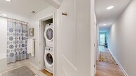 Located on East Main Street in Richmond, Virginia, this efficient and thoughtfully designed one-bedroom, one-bathroom residence offers a modern living experience across a single floor. The open-concept kitchen and living room serve as the heart of the home, featuring white shaker cabinetry, a decorative tile backsplash, stone-look countertops, stainless steel appliances including a refrigerator, range, microwave, and dishwasher, and a center island with bar seating. The living area is bright and airy, with large windows and a glass-panel door that floods the space with natural light and provides direct access to the private balcony, which offers serene, tree-lined views. Light hardwood flooring runs throughout the main living spaces, adding warmth and continuity. The bedroom is a calm retreat, fitted with ceiling fan, carpet flooring, and a clerestory window that draws in additional natural light. A dedicated closet provides convenient storage. The full bathroom features a tiled tub-shower combination, a vanity with ample counter space, and tile flooring. A utility room with a stacked washer and dryer adds in-unit convenience. A hallway connects all areas seamlessly, completing this clean and functional layout.
