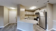 Located at 1300 Beaver Ruin Rd in Norcross, Georgia, this single-floor residence offers a thoughtfully designed layout with functional living spaces throughout. The open-concept living and dining area is finished with durable wood-look vinyl plank flooring and neutral beige walls accented by white chair rail molding, creating a clean and cohesive aesthetic. Recessed lighting adds a modern touch to the space.

The kitchen is a standout feature, equipped with stainless steel appliances including a refrigerator, electric range, microwave, and dishwasher. White cabinetry provides ample storage, while a curved peninsula with a light stone-finish countertop serves as a natural divider between the kitchen and living area. A double sink and textured ceiling complete the kitchen's practical design.

The bedroom features plush wall-to-wall carpeting, a ceiling fan with light fixture, and a window dressed with blinds that allows for natural light. The bathroom is fitted with a tiled tub-and-shower combination, a white vanity with stone-finish countertop, and tile-look flooring.

A dedicated laundry area houses a full-size washer and dryer with overhead wire shelving for added storage. Throughout the residence, consistent neutral tones and wood-look flooring create a unified, move-in-ready environment.