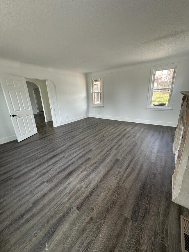 Sala de estar sin amueblar con pisos de madera oscura/estilo madera y techo texturizado. - 1247 N Florissant Rd