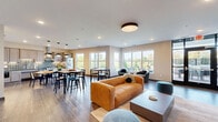 Located at 4631 Rosemary Way in Hugo, Minnesota, this thoughtfully designed single-floor space seamlessly integrates a living room, dining room, and kitchen into one cohesive, open-plan layout. Rich wood-look flooring flows throughout, anchoring the contemporary aesthetic.

The living room is a welcoming focal point, highlighted by a striking feature wall finished in muted teal board-and-batten paneling, a tiled fireplace with a wood-accented surround, and a wall-mounted television. Floor-to-ceiling glass doors and large windows bathe the space in natural light while providing direct access to an outdoor patio area, extending the living experience outside.

The kitchen is well-appointed with light gray shaker-style cabinetry, a shimmering tile backsplash, stainless steel appliances including a range with hood and French door refrigerator, and generous counter space. Pendant dome lights illuminate a substantial dining table, creating a warm and functional eat-in area.

A cozy banquette nook with a round pedestal table and pendant lighting offers an intimate dining alternative. Large picture windows throughout frame lush greenery and mature trees, bringing the outdoors in. The overall ambiance is modern, calm, and inviting, with a carefully curated palette of neutral tones accented by soft blues and warm wood details.
