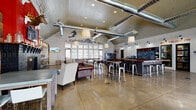 Located at 5877 N Nevada Ave in Colorado Springs, CO, this single-floor community clubhouse delivers a vibrant, adventure-inspired gathering space that blends comfort and activity. The open-plan interior features soaring vaulted ceilings with exposed silver ductwork and wood-paneled accents, anchored by polished concrete floors that run throughout. Large, multi-pane windows flood the space with natural light and offer views of the surrounding outdoor amenity areas.

The main lounge area is thoughtfully arranged with a mix of leather sofas, wingback chairs in rich terracotta tones, and industrial-style bar stools surrounding a central counter with a chalkboard menu backdrop. A wood-burning fireplace framed by reclaimed shiplap paneling and rustic décor, including mounted antler displays, adds a warm, lodge-like character to one section of the room.

The game area is well-equipped with a ping-pong table, shuffleboard, flat-screen televisions, and a Pepsi beverage station. A dedicated workout room is accessible from the main floor. Wall murals depicting mountain biking and skiing silhouettes, along with vintage license plate displays and Colorado mountain scenery cutouts, reinforce the space's bold outdoor-recreation theme throughout.