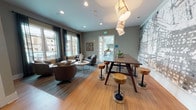 Located at 3 Woodcock Rd in Savannah, Georgia, this single-floor community clubhouse combines contemporary design with welcoming, functional spaces. The grand entrance lobby immediately impresses with soaring double-height ceilings clad in warm natural wood, floor-to-ceiling glass walls that flood the interior with natural light, and views of the surrounding greenery. A striking stone fireplace wall anchors the main lounge, where teal upholstered sofas and a live-edge wood coffee table create an inviting gathering space. Polished concrete flooring and a sliding barn door add architectural interest throughout.

Adjacent to the lobby, a secondary lounge area features warm hardwood flooring, rich brown leather swivel chairs, and large windows framed by sheer dark drapery that overlook outdoor amenities. This area transitions seamlessly into a co-working and social hub, where a substantial live-edge communal table with built-in power, surrounded by natural wood stools, sits beneath a bold abstract map mural. A beverage station with a mini-fridge, cabinetry, and a wall-mounted flat-screen television complete this multifunctional zone. A dedicated reception area and workstation with computer access are also on-site, making this clubhouse a well-rounded space for both relaxation and productivity.