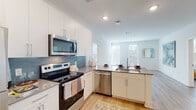 Located at 72 Milton Ave SE in Atlanta, Georgia, this single-floor residence offers a thoughtfully designed layout with contemporary finishes throughout. The open-concept kitchen serves as the heart of the home, featuring white shaker cabinetry that extends to the ceiling, a blue subway tile backsplash, quartz countertops, and a full suite of stainless steel appliances including an electric range, over-the-range microwave, dishwasher, and refrigerator. A peninsula with an integrated sink provides additional prep space and casual seating, flowing seamlessly into a bright living area bathed in natural light from large windows. Light wood-style flooring runs throughout the main living areas, adding warmth and continuity to the open floor plan. The bedrooms are carpeted and well-lit, each featuring large windows with outdoor views and ample space for furnishings. Two bathrooms serve the home, one with a soaking tub and shower combination and a wide vanity with quartz countertops, and another featuring a glass-enclosed shower, single vanity, and direct access to a walk-in closet. Clean white walls, recessed lighting, and a neutral color palette give the entire residence a bright, modern ambiance suited for comfortable everyday living.