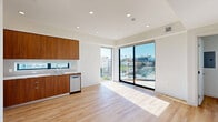 This 490 square foot apartment in Los Angeles offers a well-designed living space on a single floor. The unit features a modern kitchen with sleek wood cabinetry, stainless steel appliances, and a convenient layout. The kitchen includes a built-in microwave, electric range, and dishwasher, complemented by white quartz countertops and a narrow window for natural light.

The spacious bedroom, measuring 130 square feet, provides ample space and is enhanced by large windows offering city views. The apartment boasts light wood flooring throughout, creating a cohesive and bright atmosphere. Large windows in the living area flood the space with natural light and provide panoramic views of the Los Angeles cityscape.

A standout feature is the private balcony, accessible through sliding glass doors, offering an outdoor extension of the living space with glass railings for unobstructed views. The apartment's design maximizes space efficiency while maintaining an open, airy feel. Located at 10425–10431 Santa Monica Blvd, this unit combines modern urban living with the convenience of a central Los Angeles location.