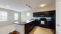 This single-floor residence offers a well-organized layout with distinct living, kitchen, bedroom, and bathroom areas. The kitchen is a standout feature, designed with rich dark cabinetry extending from floor to ceiling and outfitted with a full suite of black appliances, including a gas range, built-in microwave, dishwasher, and refrigerator. Dark countertops complement the cabinetry throughout, and a peninsula with an integrated sink provides additional workspace while opening toward the adjacent dining and living areas. Track lighting overhead brightens the kitchen, which also benefits from multiple windows that bring in natural light. The open living area is generously proportioned, finished with neutral carpet, and connects seamlessly to the kitchen via the peninsula. A separate dining nook sits adjacent to the kitchen, also carpeted and naturally lit. The bedrooms are quiet and spacious, featuring soft carpet, neutral walls, and ample natural light from large windows. Two bathrooms serve the unit; both feature light tile flooring, white vanities with under-sink storage, and well-lit mirrors. One bathroom includes a sliding-door walk-in shower, while the other offers a functional full layout. The overall palette of neutral tones and contrasting dark finishes gives the space a clean, cohesive aesthetic throughout.