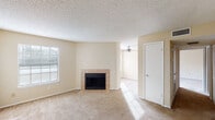 This single-story residence offers a well-organized layout designed for comfortable everyday living. The entry foyer transitions from hardwood-style flooring into the carpeted main living area, which is anchored by a tile-surround fireplace and flanked by a large window that allows natural light to fill the room. A ceiling fan in the adjoining area provides additional airflow and illumination, connecting the living space to the rest of the unit seamlessly.

The kitchen is designed with functionality in mind, featuring warm wood cabinetry, granite-look countertops, and a peninsula breakfast bar that opens toward the living and dining area. Black appliances — including a refrigerator, electric range, and overhead exhaust — complete the kitchen's cohesive look. A ceiling-mounted light fixture adds brightness to the space.

The bedroom is a well-proportioned, carpeted room with a large window that invites natural light and features neutral warm-toned walls consistent throughout the unit. Textured ceilings are present in all rooms, adding a classic touch to the overall aesthetic.

The unit's warm beige color palette, soft carpet flooring, and practical layout create a welcoming and functional living environment suited for a range of occupants.