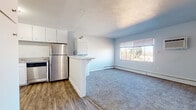 This single-floor unit offers a functional and well-organized layout that maximizes everyday comfort. The open-concept kitchen flows seamlessly into the living area, creating a connected and practical living space. The kitchen is outfitted with stainless steel appliances — including a refrigerator, electric range, and dishwasher — complemented by white cabinetry, granite-look countertops, and durable wood-look vinyl plank flooring. A peninsula with a breakfast bar divides the kitchen from the carpeted living area, which features a wall-mounted air conditioning unit, a baseboard heating system, and a large window that invites natural light and outdoor views.

Adjacent to the kitchen, a stacked in-unit washer and dryer provides added convenience. The bedrooms are carpeted and bright, each featuring windows with outdoor views and baseboard heating. The layout provides a comfortable and private retreat in each room. The bathroom is finished with white tile wainscoting, a bathtub, and wood-look vinyl flooring, offering a clean and classic aesthetic throughout. Overall, this unit combines practical features with a light, neutral palette to create a welcoming and livable space.