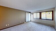 Located at 14319 Valley View Rd in Eden Prairie, Minnesota, this single-floor unit offers a straightforward, functional layout spread across several distinct spaces. The living area is generously proportioned, featuring soft carpeting, a textured ceiling, and a wall-mounted air conditioning unit. Large windows dressed with vertical blinds allow ample natural light to filter in, while a sliding glass door provides direct outdoor access and views of the surrounding greenery. Baseboard heaters run along the exterior walls, ensuring consistent warmth throughout.

The galley-style kitchen is efficiently arranged, featuring dark wood cabinetry, a double-basin sink with updated faucet, light-toned countertops, and tile-style flooring. White appliances, including a refrigerator, range, and dishwasher, are neatly integrated along the kitchen's length.

The bedrooms are carpeted and well-lit, each benefiting from windows with vertical blinds and baseboard heating. One bedroom includes a set of louvered bifold closet doors, offering organized storage. The overall layout, as seen in the 3D floor plan, includes a functional hallway connecting the kitchen, bedrooms, and living spaces, creating a cohesive and navigable interior throughout.