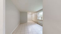 Located at 437 Jarvis St, Unit 110 in Toronto's vibrant Church-Wellesley neighbourhood, this two-bedroom, one-bathroom unit offers a practical and well-organized single-floor layout. The floor plan is structured along a linear corridor connecting all rooms, creating a clear and efficient flow throughout the space.

The living room features large windows with exterior views of surrounding greenery, allowing natural light to fill the space. White ceramic tile flooring and baseboard heating complete the room's functional design.

Both bedrooms are finished with light-toned laminate hardwood flooring and neutral grey walls, contributing to a clean, understated aesthetic. The primary bedroom offers a window with an outdoor view, a sliding closet, and baseboard heating. The second bedroom also includes a window and closet storage.

The bathroom is finished with white ceramic wall tiles and includes a full soaker tub with an overhead shower, a vanity with storage, and a small frosted window for ventilation. The laundry area features white cabinetry and a laminate countertop, providing added utility. A connecting hallway ties all areas of the unit together, completing this straightforward and functional urban residence.