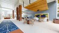 Located at 6050 Harbour Glenn Dr in Midlothian, VA, this generously sized covered outdoor amenity space is designed for community gathering and recreation. The single-level layout is defined by a striking combination of warm natural wood ceiling slats, bold brick columns, and cool gray horizontal lap siding that together create a welcoming, modern aesthetic.

At the heart of the space is a full shuffleboard court, providing a focal point for active recreation. Multiple seating zones are thoughtfully arranged throughout, including casual lounge areas with upholstered sofas and armchairs, small round tables with side chairs for intimate gatherings, and a long communal dining table accommodating larger groups.

A standout entertainment wall features dual large flat-screen TVs flanked by living green panels and natural wood accents, creating an inviting area to gather. Overhead infrared heaters are mounted to extend year-round usability. The space opens on multiple sides to the surrounding landscape, offering views of mature trees and manicured grounds that enhance the sense of openness and connection to the outdoors. The polished concrete flooring ties the entire area together, giving it a clean, contemporary feel suitable for a broad range of social and recreational activities.