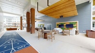 Located at 6050 Harbour Glenn Dr in Midlothian, VA, this generously sized covered outdoor amenity space is designed for community gathering and recreation. The single-level layout is defined by a striking combination of warm natural wood ceiling slats, bold brick columns, and cool gray horizontal lap siding that together create a welcoming, modern aesthetic.

At the heart of the space is a full shuffleboard court, providing a focal point for active recreation. Multiple seating zones are thoughtfully arranged throughout, including casual lounge areas with upholstered sofas and armchairs, small round tables with side chairs for intimate gatherings, and a long communal dining table accommodating larger groups.

A standout entertainment wall features dual large flat-screen TVs flanked by living green panels and natural wood accents, creating an inviting area to gather. Overhead infrared heaters are mounted to extend year-round usability. The space opens on multiple sides to the surrounding landscape, offering views of mature trees and manicured grounds that enhance the sense of openness and connection to the outdoors. The polished concrete flooring ties the entire area together, giving it a clean, contemporary feel suitable for a broad range of social and recreational activities.