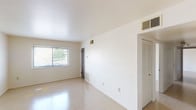 This single-floor unit offers a straightforward, functional layout with a clean, neutral aesthetic throughout. The living area is generously proportioned, featuring large windows fitted with horizontal blinds that allow natural light to fill the space and provide views of surrounding greenery. Light-colored tile flooring extends across the main living spaces, reflecting natural light and contributing to a bright, open feel. White walls and smooth ceilings with centrally placed HVAC vents maintain a consistent, minimalist appearance. A closet with louvered doors adds practical storage to the living area.

Multiple additional rooms share the same tile flooring and white wall finish, each equipped with windows that bring in natural light and outdoor views. These rooms offer flexible use and connect fluidly to the rest of the unit.

The kitchen is compact and efficiently arranged in an L-shape, featuring warm wood-toned cabinetry with ample upper and lower storage, light-colored countertops, and a stainless steel sink. Vinyl tile flooring grounds the space practically.

The bathroom includes a full tub and shower combination with white subway tile surround, a toilet, and a wood-toned vanity with an integrated sink and wall-mounted mirror. Overall, the unit presents a clean, move-in ready environment with consistent finishes throughout.