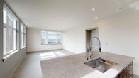 This well-designed single-floor unit offers a clean, contemporary aesthetic with a neutral color palette and light wood-look flooring that flows seamlessly throughout the space. The open-concept living and kitchen area serves as the heart of the unit, bathed in natural light from a large picture window that frames outdoor views. The kitchen is a standout feature, showcasing a central island with a granite-topped countertop, an undermount stainless steel sink, and a professional-style pull-down faucet. Rich, dark wood grain cabinetry lines the walls, complemented by a stylish mosaic tile backsplash and a full suite of stainless steel appliances, including a range, over-the-range microwave, and refrigerator. The spacious bedroom is filled with natural light from dual windows offering outdoor views, and includes a ceiling fan for added comfort. Two bathrooms serve the unit, each featuring granite-topped vanities with undermount sinks and dark cabinetry. One bathroom includes a combination tub and shower with chrome fixtures and a rain-style showerhead, while the second offers a similarly appointed tub-shower setup. Recessed lighting throughout the unit adds to the bright, polished ambiance of this modern residence.