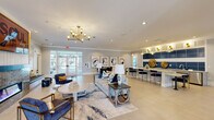 Located at 4692 E Ponce de Leon Ave in Stone Mountain, Georgia, this single-story community clubhouse offers a thoughtfully designed gathering space with a cohesive modern aesthetic. The entry opens into a grand vaulted foyer framed by white brick columns, setting an elegant tone before flowing into the main lounge area. The central lounge is anchored by a striking wood-surround fireplace with a stone hearth, accompanied by curated seating arrangements, a geometric gold wall installation, and a built-in bench nook. A bold gold chandelier adds warmth and sophistication overhead. Adjacent to the lounge, a stylish wet bar features a large granite-topped island with navy velvet barstools, bold blue tile accents, and gold pendant lighting, creating a vibrant social hub. Multiple dining vignettes are scattered throughout, including a casual seating area with a wall-mounted TV and a Scrabble board, and a refined dining nook adorned with a series of large abstract artworks. A well-equipped kitchenette with wood cabinetry, granite countertops, and a coffee station supports the dining areas. The business center provides multiple computer workstations with ample natural light from surrounding windows. Light tile flooring, neutral gray walls, and curated artwork unify the space with a polished, contemporary character.