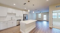 Located at 1023 Gull Ln in Melbourne, FL, this well-appointed 2-bedroom, 3-bathroom residence offers a thoughtfully designed single-floor layout that balances comfort and modern style. The open-concept living area seamlessly connects the kitchen, dining, and living spaces, all finished with light wood-look flooring that creates a warm, cohesive feel. The kitchen is a standout feature, showcasing crisp white cabinetry extending to the ceiling, a large center island with a quartz countertop, subway tile backsplash, and a full suite of stainless steel appliances, including a refrigerator with ice maker, range, microwave, and dishwasher. Pendant lighting above the island adds a modern touch. The living area is bright and open, benefiting from natural light and a ceiling fan. Both bedrooms are carpeted and well-sized, each with ceiling fans. The spacious primary bedroom connects to a generously sized en-suite bathroom featuring a glass-enclosed walk-in shower with large-format tile, a white vanity with quartz countertop, and an illuminated mirror. The secondary bathroom offers a tiled tub-shower combo with equally refined finishes. Three closets, including a walk-in with wire shelving, provide ample storage. A private balcony and in-unit laundry area complete this move-in-ready home.