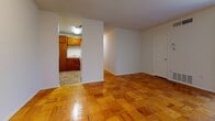 Located at 2834 Broad Rock Blvd in Richmond, Virginia, this single-floor unit offers a straightforward and functional layout across several well-defined spaces. The living area serves as the heart of the unit, showcasing warm-toned parquet wood flooring in a distinctive checkerboard pattern that extends throughout the main living spaces. A large sliding glass door dressed with vertical blinds allows natural light to fill the room and provides an outdoor view, while a wall-mounted HVAC vent ensures year-round comfort. The adjoining area opens conveniently to the kitchen, which features warm wood cabinetry, light countertops, tile flooring, a white electric range with coil burners, and a sink — providing all the essential elements for everyday cooking and meal preparation. In-unit laundry connections are also present within the kitchen space. The bedroom continues the parquet flooring theme and offers a calm, neutral atmosphere with white walls and access to additional areas of the unit. The bathroom is finished with terracotta-toned tile flooring and classic pink subway tile surrounding a full soaking tub and shower combination, complemented by a standard toilet. The overall aesthetic is clean and practical, making this a functional Richmond residence.