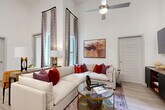 This well-appointed 2-bedroom, 2-bathroom residence in Allen, TX offers a thoughtfully designed single-floor layout that maximizes both comfort and functionality. The open-concept living, dining, and kitchen area serves as the heart of the home, highlighted by dramatically tall ceilings and floor-to-ceiling windows that flood the space with natural light. The living room features light wood-style flooring and a ceiling fan, while large draped windows frame views of the outdoors. The kitchen is a standout, boasting two-tone cabinetry in white and gray, a hexagonal tile backsplash, stainless steel appliances, white quartz countertops, and a center island with bar seating — ideal for both cooking and casual dining. The primary bedroom offers soaring ceilings, an outdoor-facing window, plush carpeting, and generous closet space. The second bedroom mirrors the airy aesthetic with tall ceilings and natural light. The primary bathroom features light wood flooring, a walk-in tiled shower, and a gray dual-sink vanity with an illuminated mirror. The second bathroom includes a tiled tub-shower combination. Additional conveniences include in-unit laundry and four closets throughout. The overall ambiance is modern, bright, and welcoming.