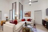 This well-appointed 2-bedroom, 2-bathroom residence in Allen, TX offers a thoughtfully designed single-floor layout that maximizes both comfort and functionality. The open-concept living, dining, and kitchen area serves as the heart of the home, highlighted by dramatically tall ceilings and floor-to-ceiling windows that flood the space with natural light. The living room features light wood-style flooring and a ceiling fan, while large draped windows frame views of the outdoors. The kitchen is a standout, boasting two-tone cabinetry in white and gray, a hexagonal tile backsplash, stainless steel appliances, white quartz countertops, and a center island with bar seating — ideal for both cooking and casual dining. The primary bedroom offers soaring ceilings, an outdoor-facing window, plush carpeting, and generous closet space. The second bedroom mirrors the airy aesthetic with tall ceilings and natural light. The primary bathroom features light wood flooring, a walk-in tiled shower, and a gray dual-sink vanity with an illuminated mirror. The second bathroom includes a tiled tub-shower combination. Additional conveniences include in-unit laundry and four closets throughout. The overall ambiance is modern, bright, and welcoming.
