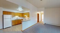 This single-floor residence offers a thoughtfully designed layout with a warm, functional aesthetic defined by consistent wood-toned trim, doors, and cabinetry throughout. The kitchen is a practical centerpiece, featuring an L-shaped arrangement of honey-toned oak cabinets, light granite-style countertops, tile flooring, a double sink, and a full suite of white appliances including a refrigerator, electric range, and dishwasher. A peninsula counter connects the kitchen to the adjacent living area, which boasts vaulted ceilings, plush carpeting, a ceiling fan, and a chandelier-lit dining nook. A separate living room offers a corner fireplace, baseboard heating, and a large sliding glass door that fills the space with natural light and provides access to an outdoor patio. The bedrooms are carpeted and bright, each featuring wood-framed windows that invite natural light, with one bedroom offering direct access to a private bathroom. The bathroom is finished with tile flooring, a vanity with under-sink storage, a lighted mirror, and a tub/shower combination. Throughout the home, consistent baseboard heating, warm neutral walls, and cohesive wood accents create a comfortable and inviting atmosphere.