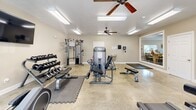 Located at 1515 Aggie Rd in Jonesboro, Arkansas, this fitness center offers a dedicated exercise space designed to support a well-rounded workout routine. The room features polished concrete flooring throughout, providing a durable and easy-to-maintain surface suited for high-activity use. Bright fluorescent lighting is complemented by multiple ceiling fans, ensuring the space remains well-lit and comfortable during workouts.

The cardio section is equipped with two treadmills, an elliptical trainer, and a stationary bike, all positioned near large windows that allow natural light to fill the room and offer views of the surrounding outdoor area. A wall-mounted flat-screen television adds an entertainment option for those logging time on cardio machines.

The strength training area features a multi-station cable machine, a dumbbell rack with a full range of free weights, and adjustable benches, providing ample options for resistance training. Interlocking foam floor mats are placed strategically under equipment to protect both the floor and users. A wall-mounted water fountain with bottle-fill capability ensures convenient hydration access.

A large interior window connects the fitness room to an adjacent common area, adding a sense of openness to the space. The neutral-toned walls and clean, functional layout create a focused and welcoming environment for exercise.