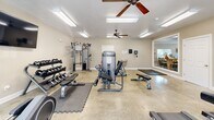 Located at 1515 Aggie Rd in Jonesboro, Arkansas, this fitness center offers a dedicated exercise space designed to support a well-rounded workout routine. The room features polished concrete flooring throughout, providing a durable and easy-to-maintain surface suited for high-activity use. Bright fluorescent lighting is complemented by multiple ceiling fans, ensuring the space remains well-lit and comfortable during workouts.

The cardio section is equipped with two treadmills, an elliptical trainer, and a stationary bike, all positioned near large windows that allow natural light to fill the room and offer views of the surrounding outdoor area. A wall-mounted flat-screen television adds an entertainment option for those logging time on cardio machines.

The strength training area features a multi-station cable machine, a dumbbell rack with a full range of free weights, and adjustable benches, providing ample options for resistance training. Interlocking foam floor mats are placed strategically under equipment to protect both the floor and users. A wall-mounted water fountain with bottle-fill capability ensures convenient hydration access.

A large interior window connects the fitness room to an adjacent common area, adding a sense of openness to the space. The neutral-toned walls and clean, functional layout create a focused and welcoming environment for exercise.