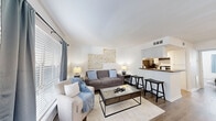 Located at 9220 Nathaniel St in Houston, TX, this well-designed 1-bedroom, 1-bathroom unit offers a comfortable and efficient single-floor layout. The open-concept living and dining area is bright and welcoming, featuring wood-look flooring throughout, neutral white walls, and large windows dressed with gray curtains that allow natural light to fill the space. A raised breakfast bar seamlessly connects the living area to the kitchen, providing a convenient casual dining option with bar stool seating.

The galley-style kitchen is efficiently laid out with crisp white cabinetry, light countertops, a stainless steel sink, and black appliances including a refrigerator and range, offering ample workspace and storage for everyday cooking.

The bedroom is a comfortable retreat with a ceiling fan, natural light from a window with blue curtains, hardwood-style flooring, and enough space to accommodate a full furniture arrangement. Two closets serve the unit, providing generous storage capacity.

The bathroom features a large vanity with a white countertop, a wide mirror, and modern light fixtures, maintaining the clean and bright aesthetic found throughout the home. A hallway connects the main living spaces to the private areas, contributing to a practical and well-organized floor plan.
