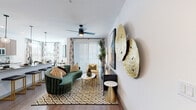 This single-floor residence showcases a carefully curated modern aesthetic throughout its well-organized layout. The living area serves as the centerpiece of the home, featuring warm hardwood-style flooring, a ceiling fan, and a sliding glass door with vertical blinds that fills the space with natural light. A curved emerald-green sofa, a marble-topped coffee table, and a statement gold sculptural wall piece lend an upscale, artistic character to the room. A sleek black credenza and large-scale canvas artwork further elevate the design.

The open-concept kitchen is equipped with stainless steel appliances, two-tone cabinetry combining warm wood uppers with clean white lowers, subway tile backsplash, and a quartz waterfall island with pendant lighting — ideal for both cooking and casual dining.

The bedroom offers a serene retreat with plush carpeting, a ceiling fan, a tufted upholstered headboard, and a bright window with sheer curtains. A sliding-door walk-in closet provides generous storage. The bathroom features a wide quartz vanity with a walnut cabinet base, an illuminated LED mirror, and hardwood-style flooring. A dedicated in-unit laundry room with full-size washer and dryer completes this thoughtfully designed home.
