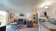 This single-floor residence offers a thoughtfully designed layout that balances functionality and comfort throughout its key living areas. The kitchen is a standout feature, equipped with stainless steel appliances including a range, microwave, and refrigerator, complemented by light wood cabinetry, gray countertops, and durable wood-look flooring. A central island with pendant lighting provides additional prep space and a natural gathering point, connecting the kitchen to the rest of the living areas.

Adjacent to the kitchen, the dining area accommodates a round table with seating for four, accented by neutral walls that create a relaxed atmosphere. The living room features plush carpeting, generous seating space, and soft ambient lighting, lending a warm and inviting feel to the area.

The two bedrooms are carpeted and well-sized, each offering natural light through sizable windows. The primary bedroom provides a tranquil retreat, while the second bedroom offers similar comfort and versatility. The bathroom is finished with wood-look flooring, a vanity with matching light wood cabinetry, and a glass-enclosed shower, reflecting the consistent design aesthetic carried throughout the home.