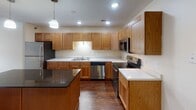 Located at 2600 S 34th St in Grand Forks, North Dakota, this single-floor residence offers a functional and comfortable layout with a thoughtfully designed interior. The kitchen is a standout feature, showcasing warm honey-toned shaker-style cabinetry that extends to the ceiling, providing generous storage throughout. Stainless steel appliances — including a refrigerator, dishwasher, microwave, and range — complement the white countertops and a central island topped with a dark granite surface, illuminated by pendant lighting overhead. Rich hardwood-style flooring runs throughout the kitchen and dining area, adding warmth and visual continuity. The open layout allows the kitchen to flow seamlessly into the living area, which transitions to plush wall-to-wall carpeting. The living room is bright and spacious, featuring a sliding glass door that opens to a private balcony, allowing for natural light and outdoor access. The bedroom is well-sized, carpeted, and lit by a window overlooking the exterior. The bathroom includes a clean, full-size soaking tub and shower combination with chrome fixtures. Recessed lighting and textured ceilings are consistent throughout the space, contributing to a cohesive and practical residential environment.