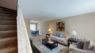 This two-story residence offers a practical and comfortable layout across two well-defined levels. The main floor features an open-concept living and dining area finished with neutral-toned walls and carpeting throughout. The living room provides ample space for seating and includes a built-in shelving unit tucked beneath the staircase, along with a large window that draws in natural light. A decorative staircase with ornamental railings connects the two floors. The adjacent dining area is illuminated by a pendant light fixture and features a sliding glass door with vertical blinds, allowing additional natural light. The kitchen is efficiently designed with white cabinetry, granite-style countertops, a double sink, and white appliances including a refrigerator, dishwasher, and range. A half bathroom is conveniently located on the main level. Upstairs, both bedrooms are generously sized with carpet flooring and ceiling fans. The primary bedroom includes a walk-in closet and an en-suite bathroom, while the second bedroom also benefits from its own full bathroom featuring a tub-shower combination. The overall ambiance is clean, neutral, and move-in ready.