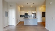 This well-appointed single-floor residence combines modern design with functional living. The open-concept layout centers around a striking kitchen, where white shaker-style cabinetry reaches toward the ceiling and is accented by a bold mosaic tile backsplash in black, white, and grey tones. A large central island with a granite countertop and undermount sink serves as both a prep space and gathering point, illuminated by a pair of pendant lights overhead. Stainless steel appliances, including a range, over-the-range microwave, and refrigerator, complete the kitchen's contemporary look. Durable wood-look flooring flows throughout the main living areas, while the spacious living room offers a ceiling fan and access to natural light through a exterior-facing door. The bedroom is carpeted and features dual windows that invite generous natural light. The primary bathroom is elegantly finished with a granite-topped vanity, white cabinetry, a glass-enclosed shower, and a doorway leading to a walk-in closet with built-in shelving. A secondary bathroom includes a soaking tub with marble-style tile surround. A dedicated in-unit laundry closet and a private entry hallway add to the convenience and comfort of this thoughtfully designed residence.