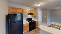 Located at 2326 Roland Dr in Monroe, NC, this single-story home presents a straightforward and functional layout supported by consistent design choices throughout. The interior is finished with warm neutral tones on the walls, complemented by white trim and textured ceilings that carry through each room.

The main living area is generously proportioned, featuring plush wall-to-wall carpeting and a ceiling fan with a light fixture. A window fitted with horizontal blinds allows natural light to filter in, while a sliding glass door on one wall provides additional brightness and access to the exterior. The space connects openly to the kitchen via a counter-height peninsula, creating a cohesive flow between the two areas.

The kitchen is equipped with warm oak cabinetry, light-toned countertops, and wood-look flooring. Black appliances—including a refrigerator and an electric range with overhead ventilation—anchor the space, while ample upper and lower cabinet storage adds practicality.

The bedrooms continue the carpeted flooring and neutral palette, each featuring windows with outdoor views of surrounding greenery. The bathroom includes a vanity with a light stone-style countertop, a large mirror, a multi-bulb vanity light fixture, and under-sink cabinetry, offering a clean and organized space.